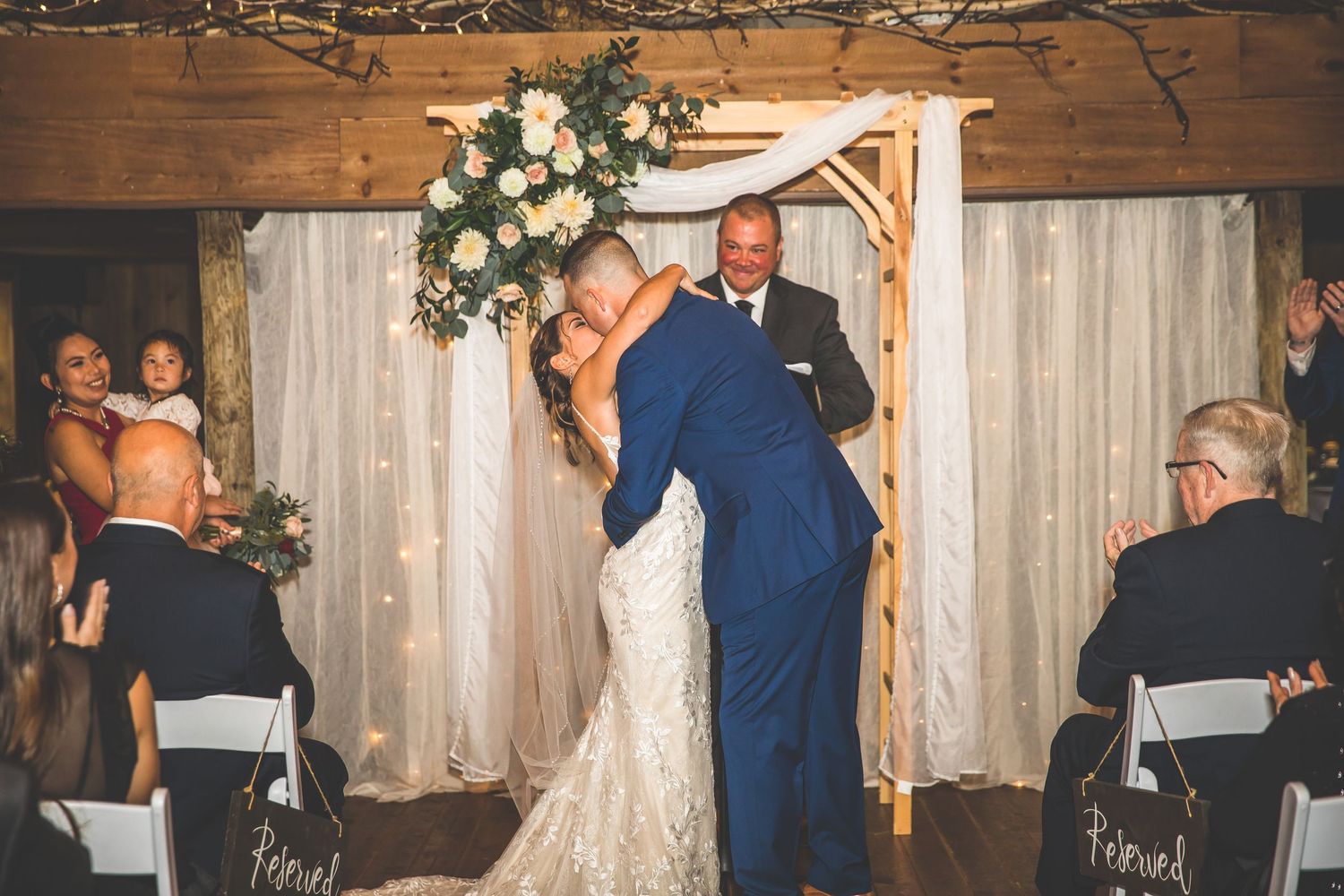 Wedding celebration in a rustic barn venue with white floral arrangements and wooden beam details.