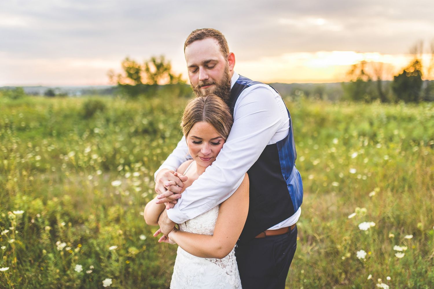 A bride and groom embrace while standing in a summer meadow with flowers.