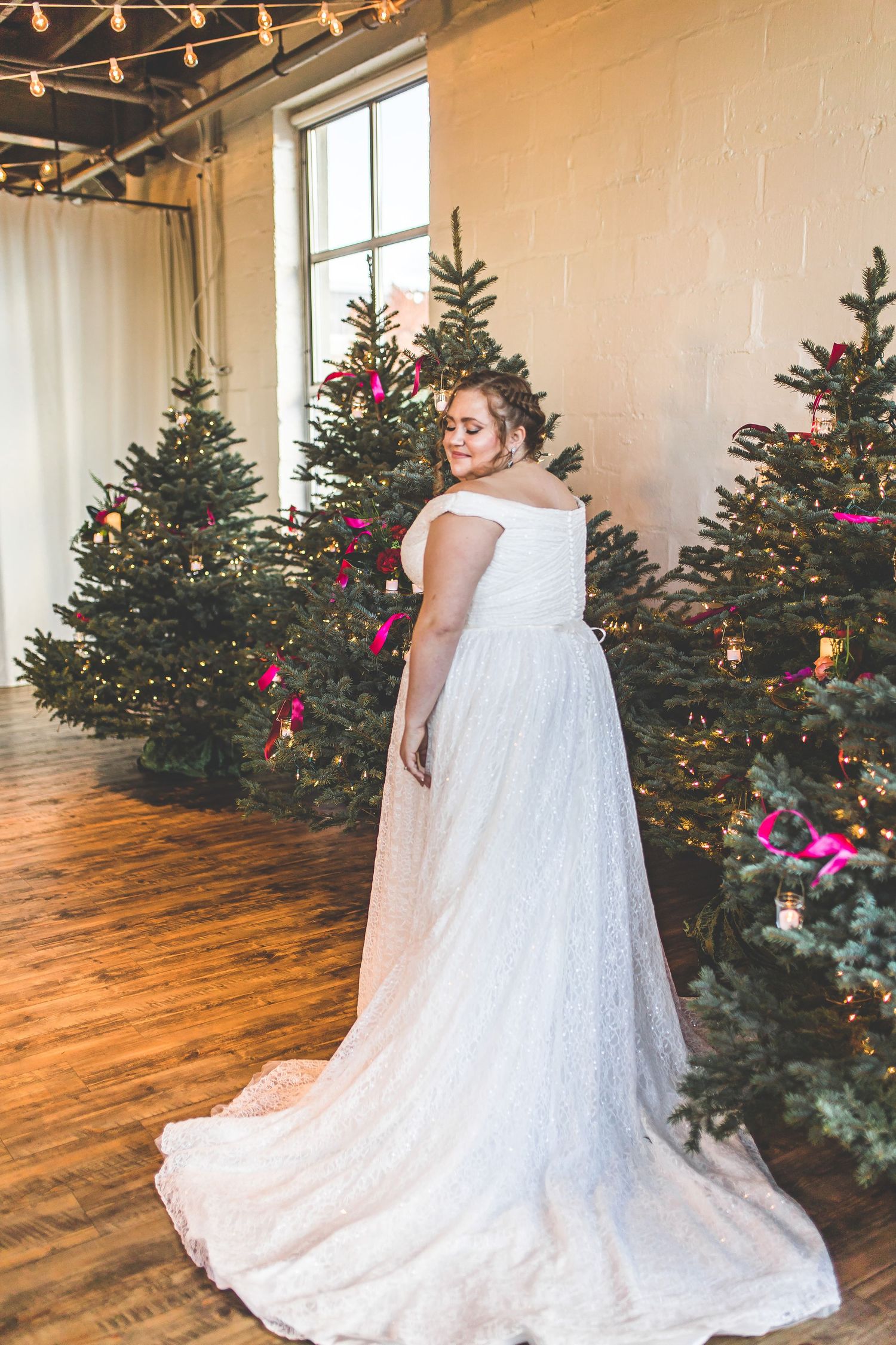 White wedding gown with lace details displayed against decorated Christmas trees.