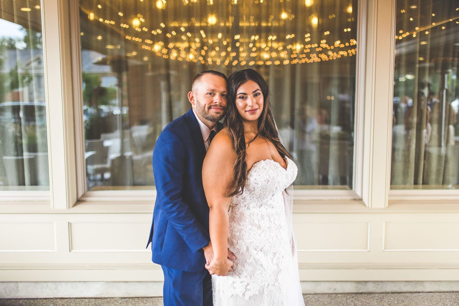 Romantic wedding couple portraits under warm string lights at venue entrance.