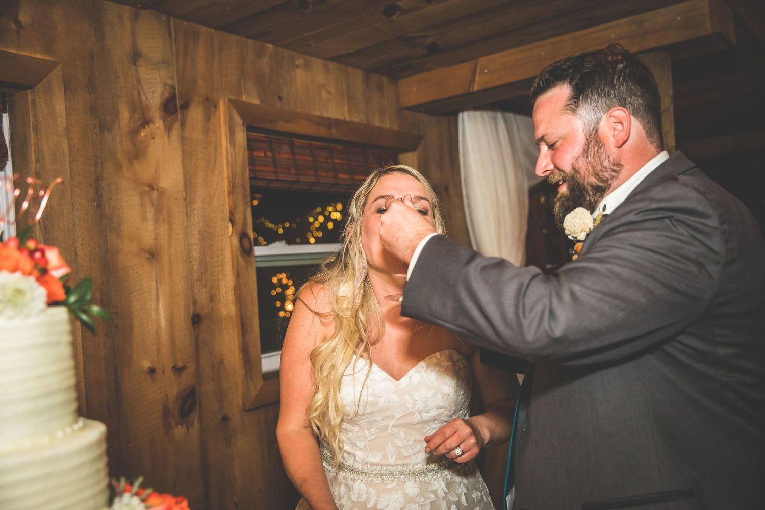 Couple shares a joyful moment while cutting their wedding cake in a wood-paneled venue.