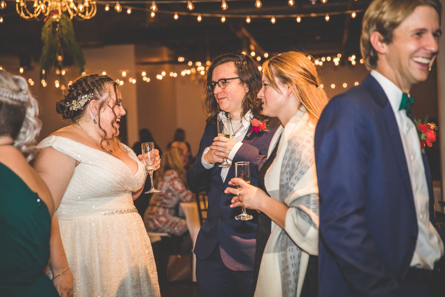 Guests mingle and celebrate at an elegant indoor wedding reception with string lights overhead.