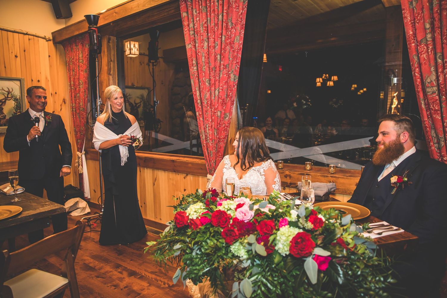 Wedding reception table adorned with red floral arrangements and festive red curtains.