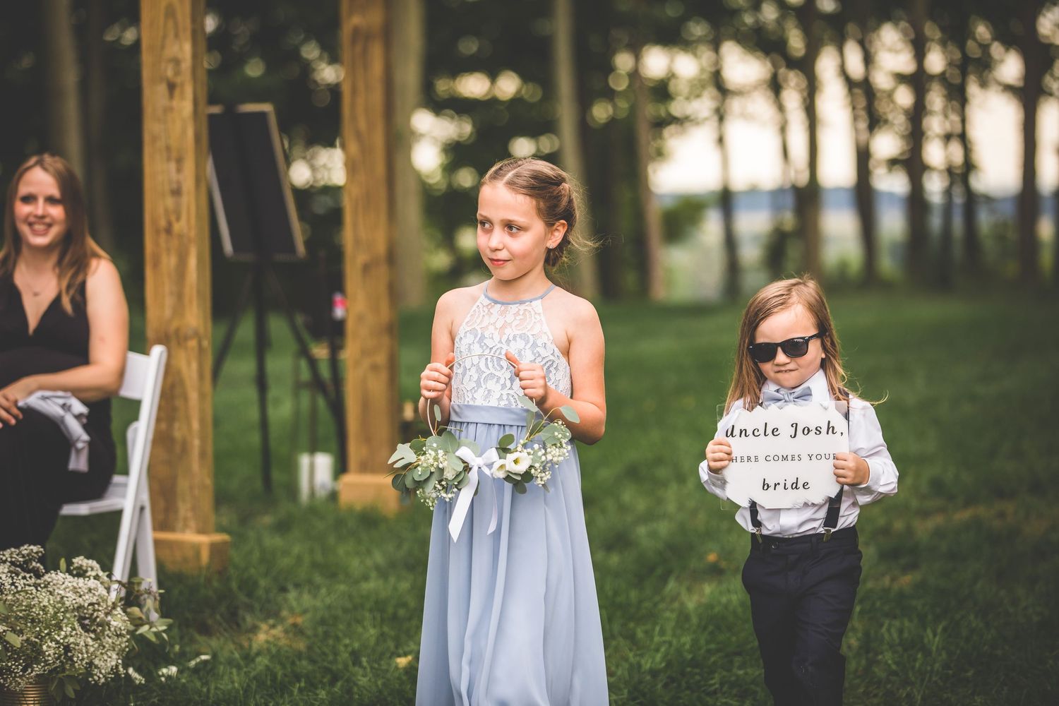Wedding attendants walking down grassy aisle between wooden posts.