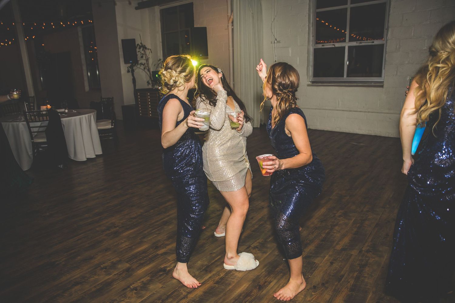 Wedding guests dancing on wooden floor under festive string lights.