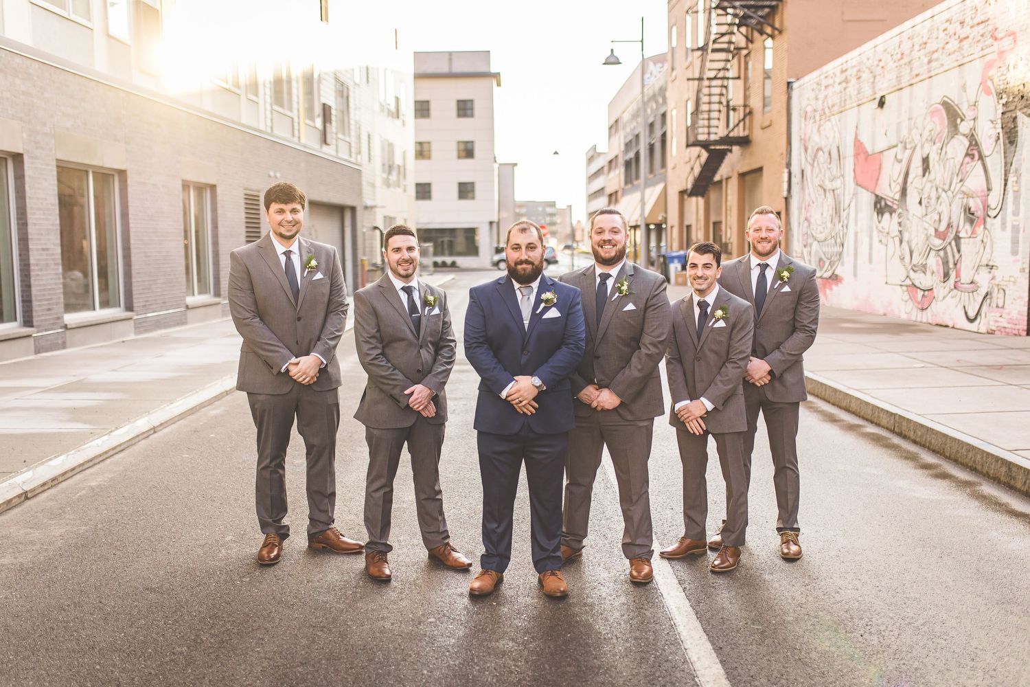Groomsmen in coordinated suits walk together through city alleyway.