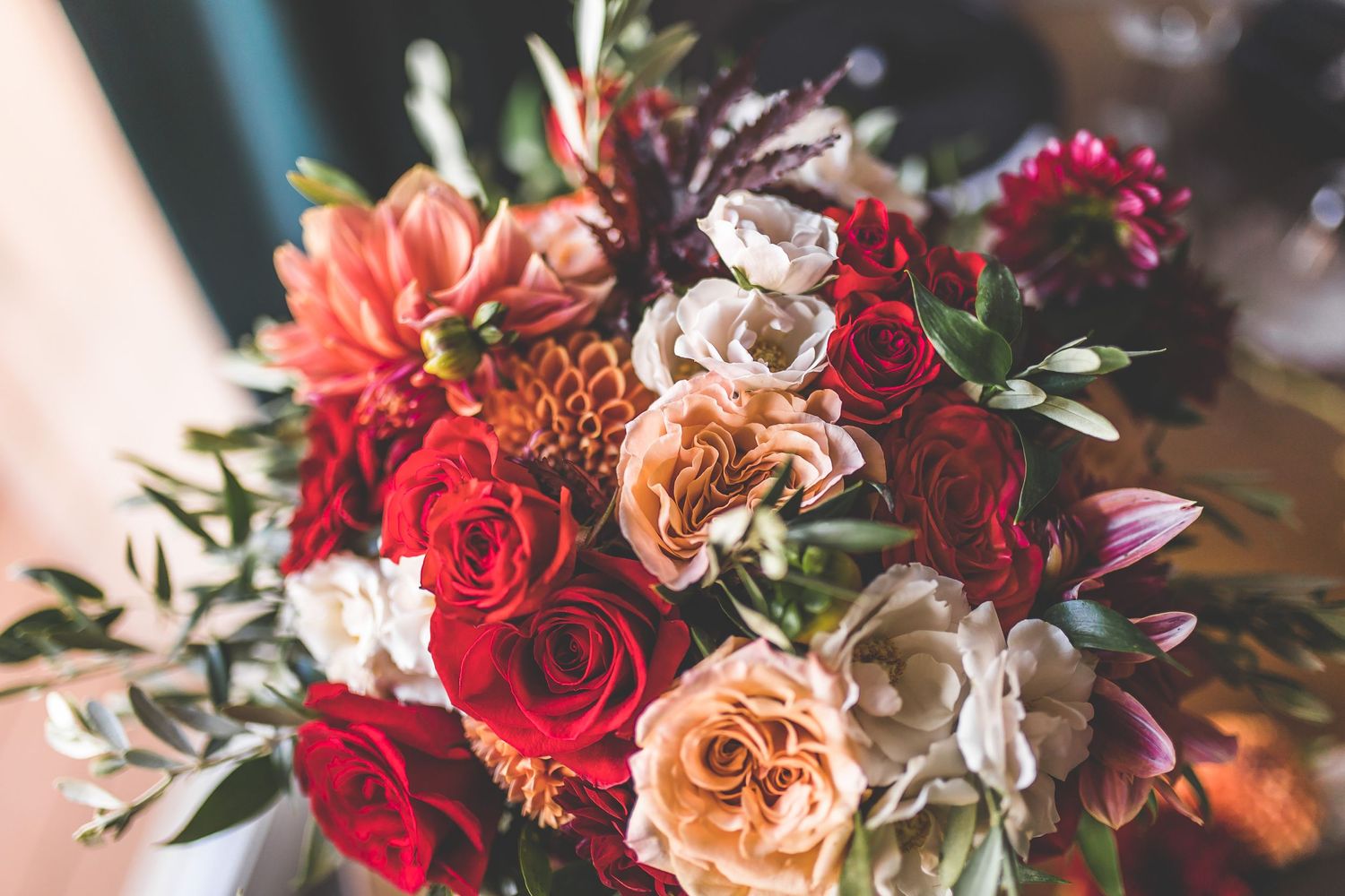 Vibrant wedding bouquet with red roses, peach flowers, and mixed florals in rich autumn colors.