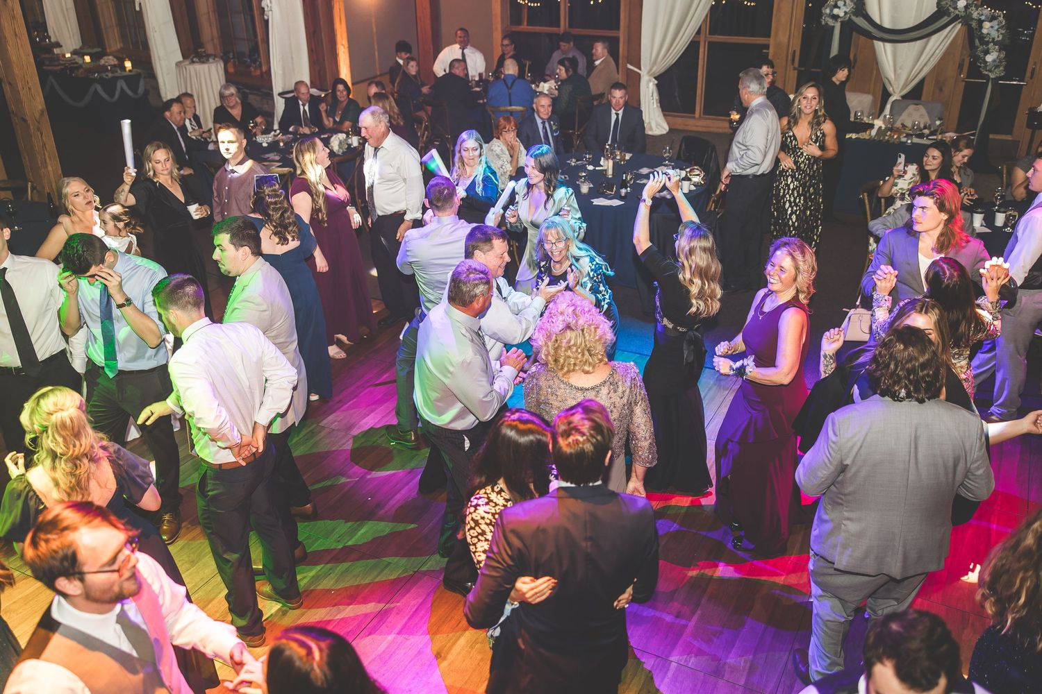 Large crowd dancing on a dimly lit dance floor with purple lighting and festive atmosphere.