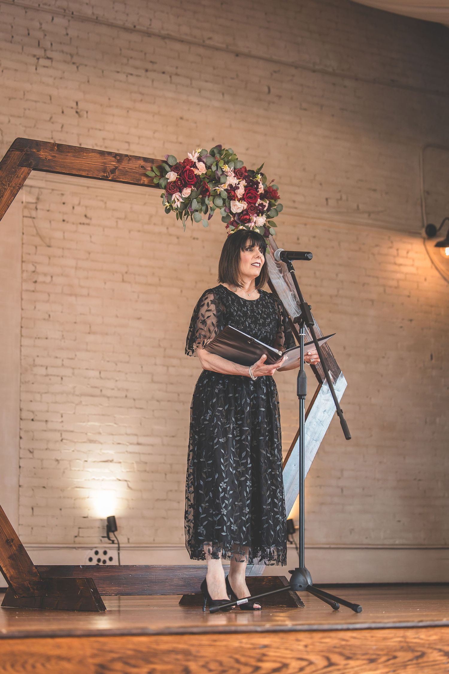 Performance stage with black lace-dressed singer against white brick wall backdrop.