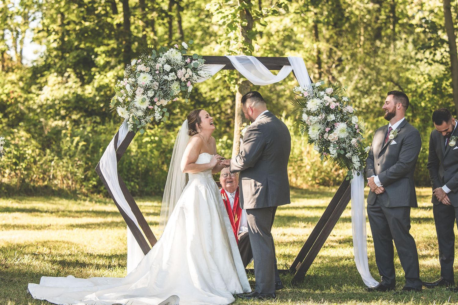 A tender moment during an outdoor wedding ceremony beneath a decorated arch.