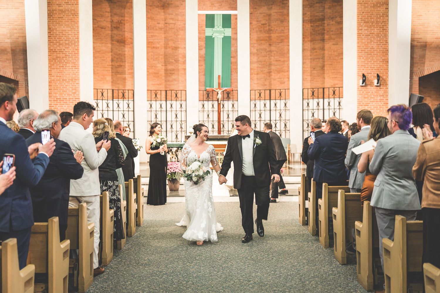 Wide view of church interior with wooden pews and brick architecture during wedding celebration.