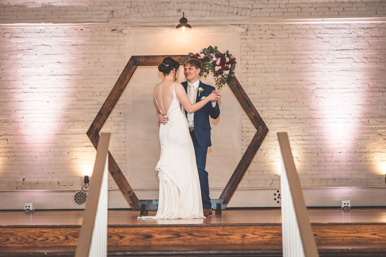 Newlyweds dance together in an industrial-chic venue with exposed brick walls.