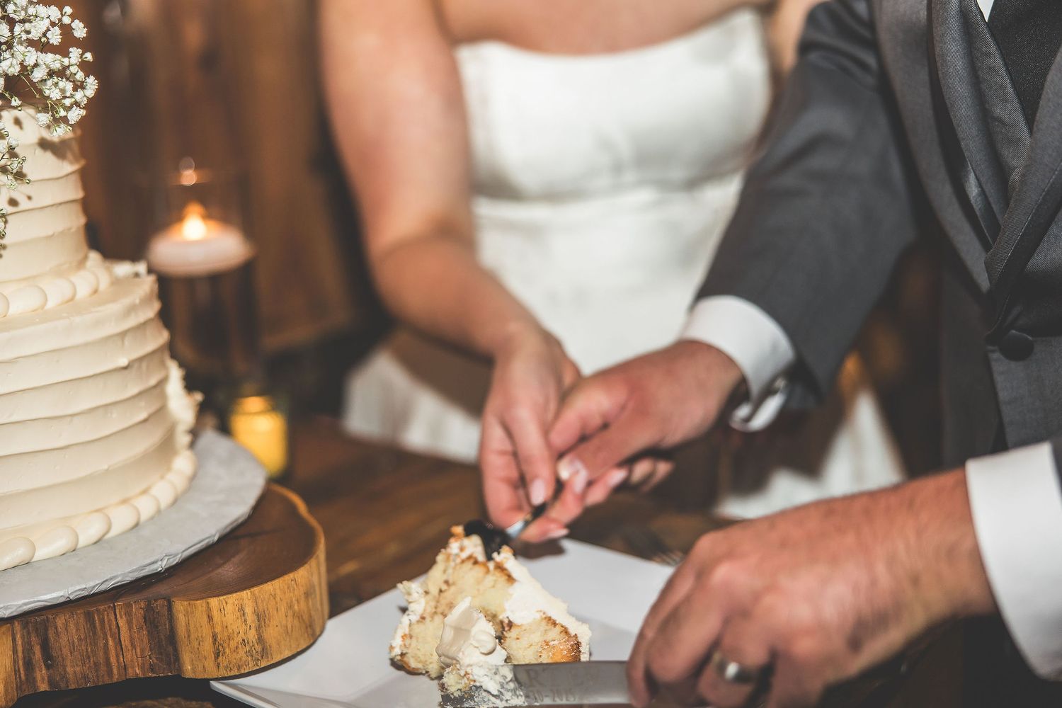 Close-up details of wedding cake cutting at rustic wooden reception venue.