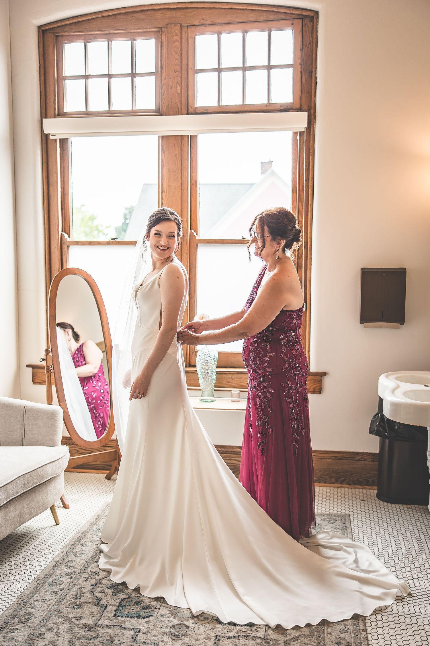 Wedding dress fitting scene showing final adjustments in room with wooden windows.