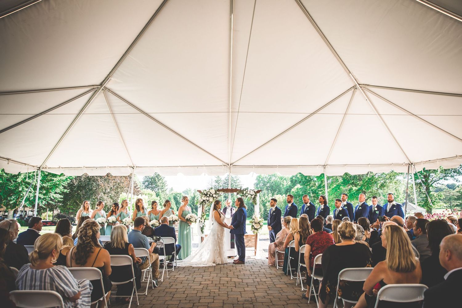 Panoramic view of wedding ceremony setup under large white tent with rows of chairs.