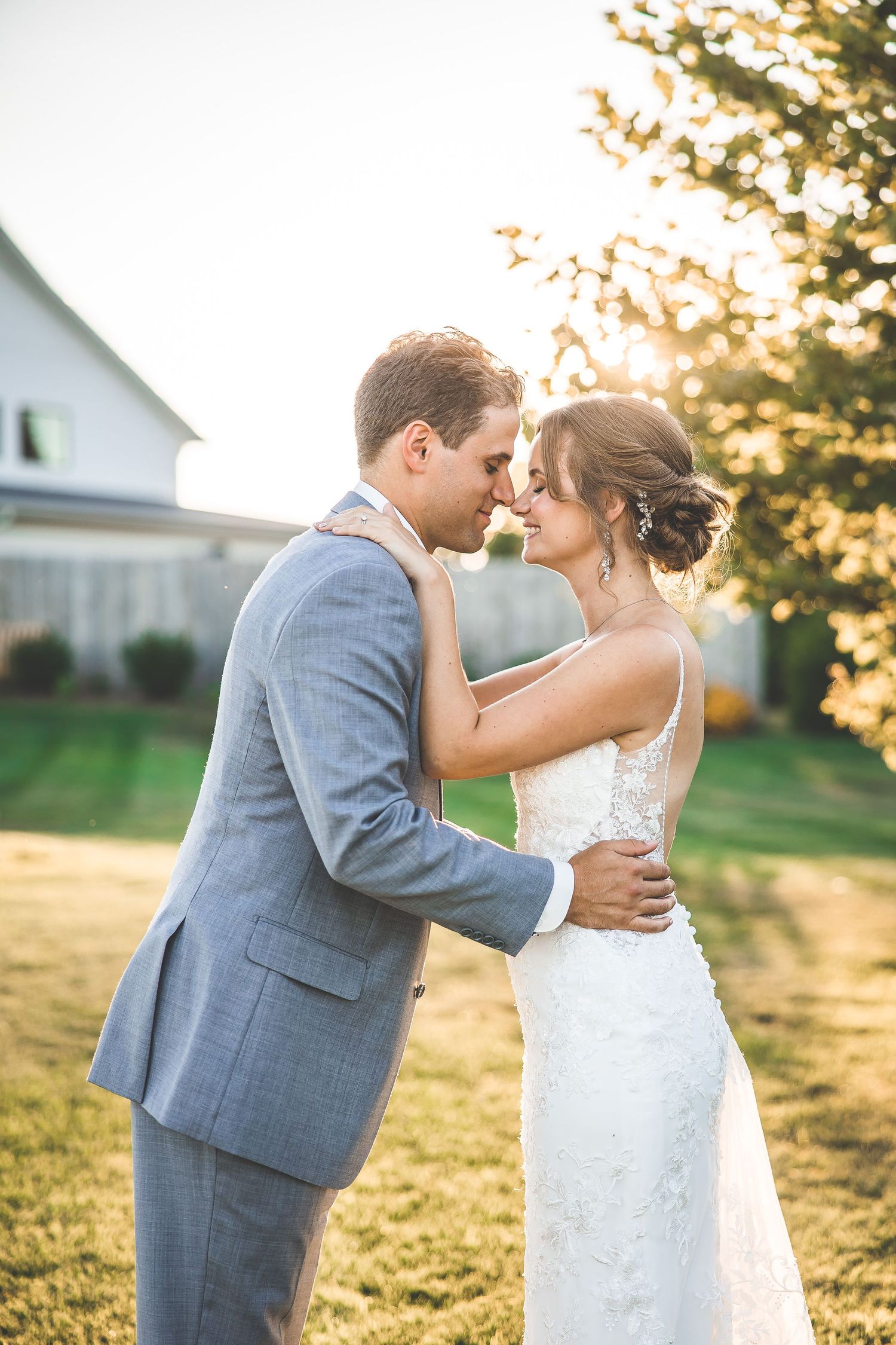 Romantic sunset wedding portrait of newlyweds embracing in formal attire on a lawn.