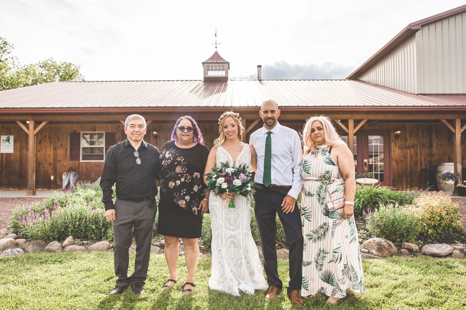 Rustic barn wedding venue exterior with wedding party posing in garden setting.