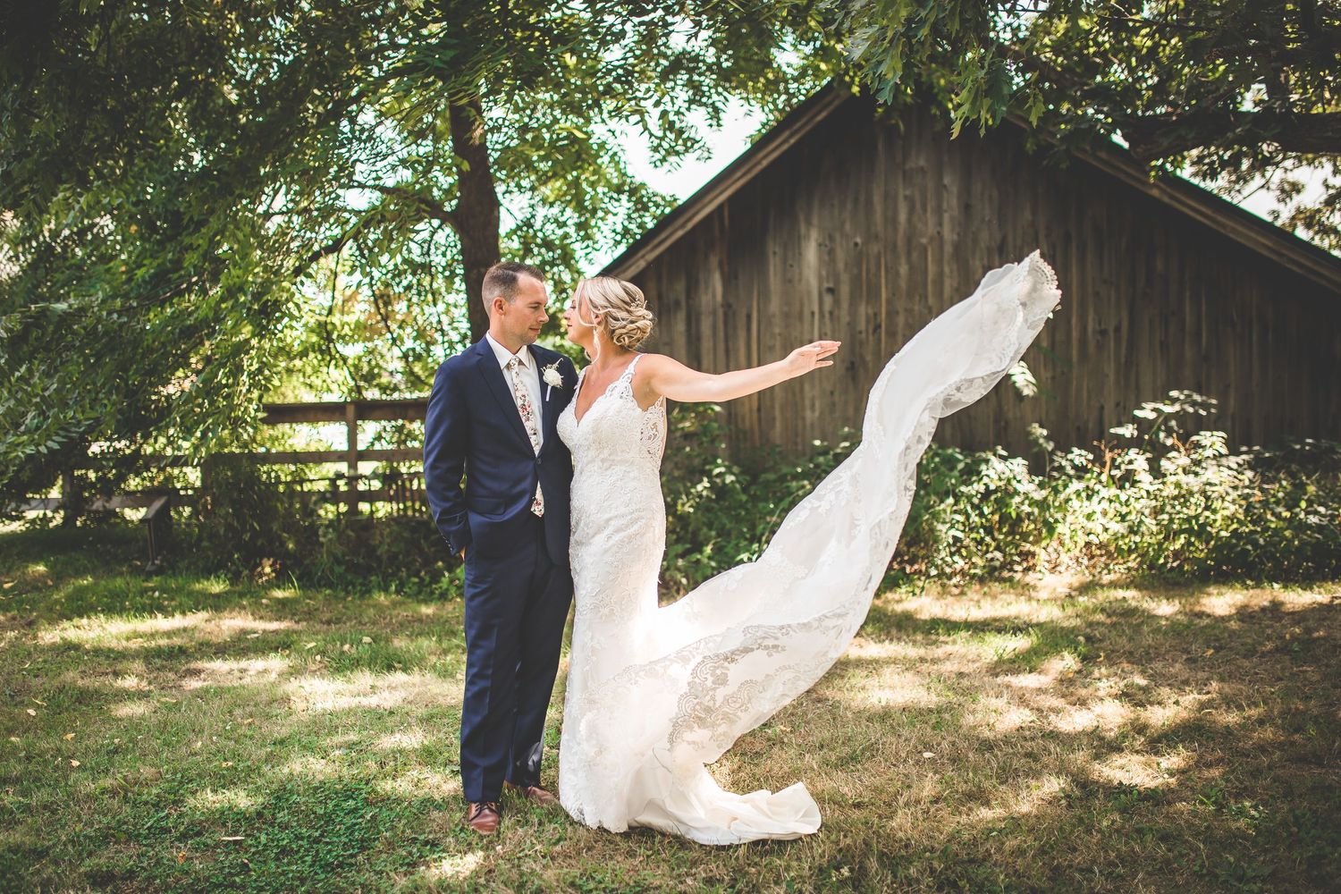 A playful wedding photo with the bride's dress flowing in the wind near a rustic barn.