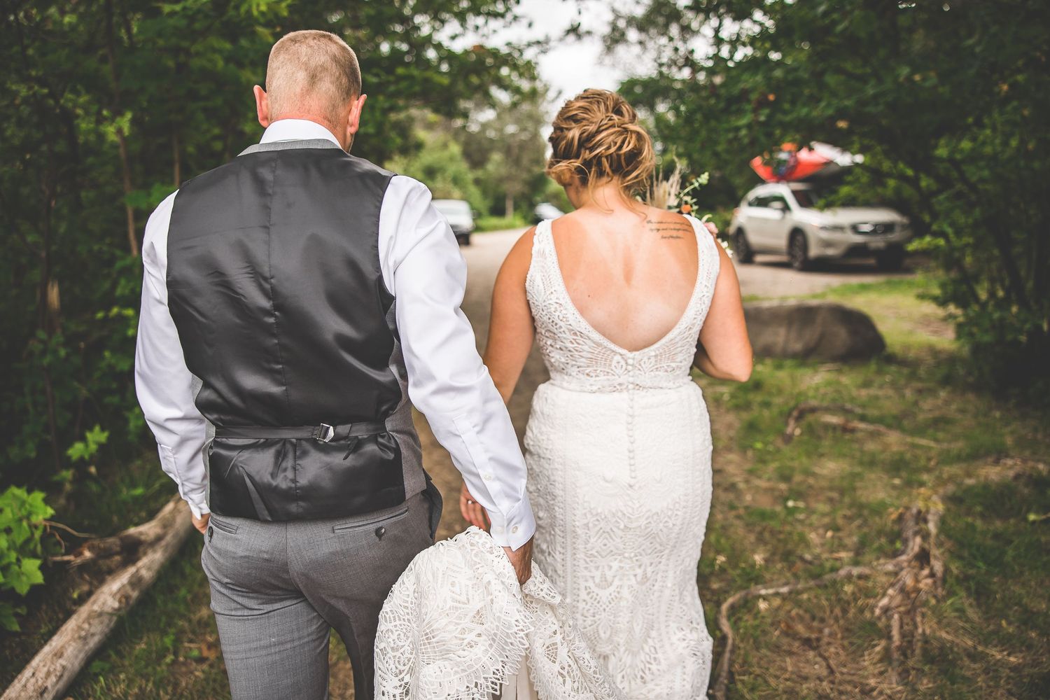 Back view of newlyweds in formal attire walking together outdoors.