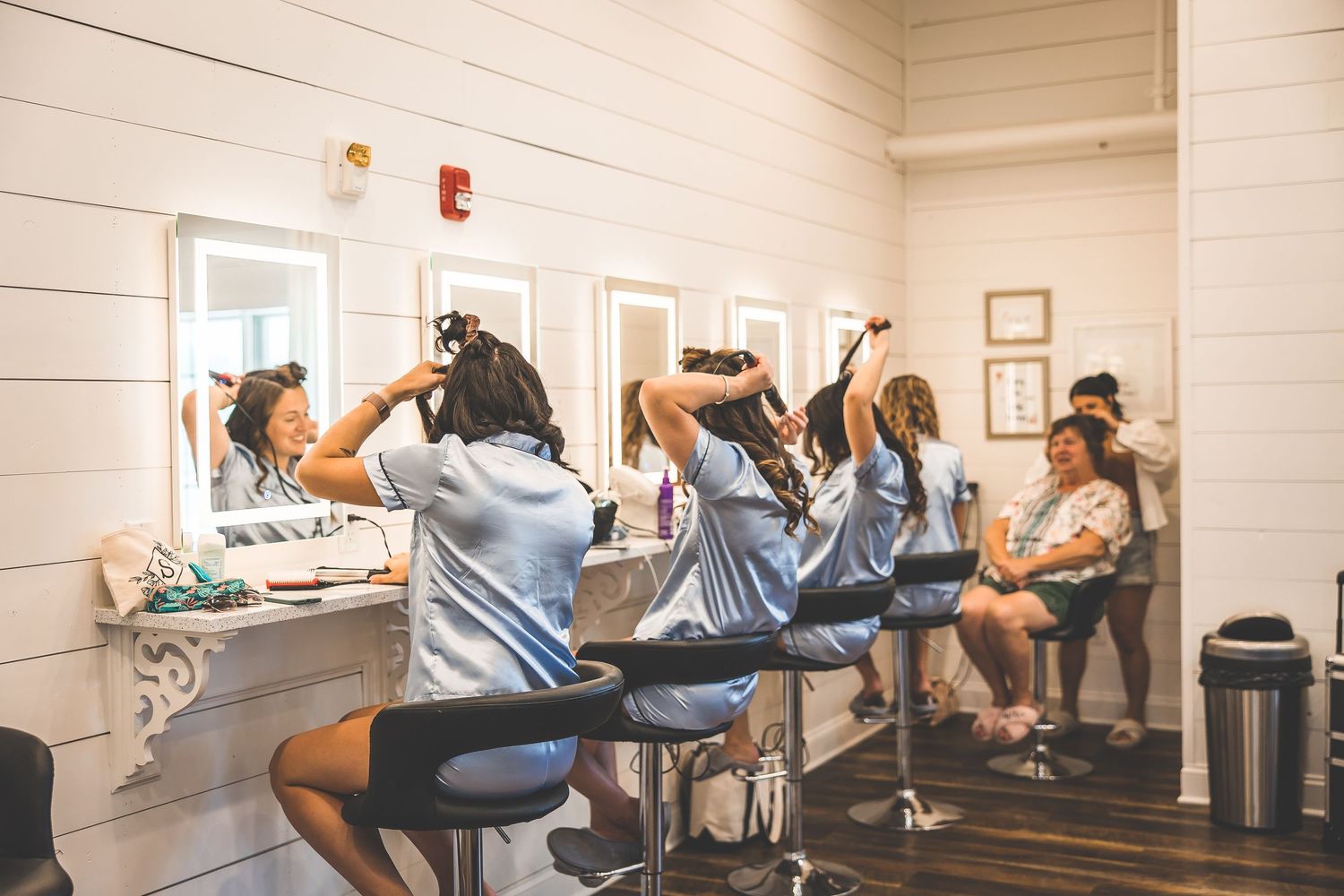 Wedding preparation scene in bridal suite with stylists working at illuminated makeup stations.