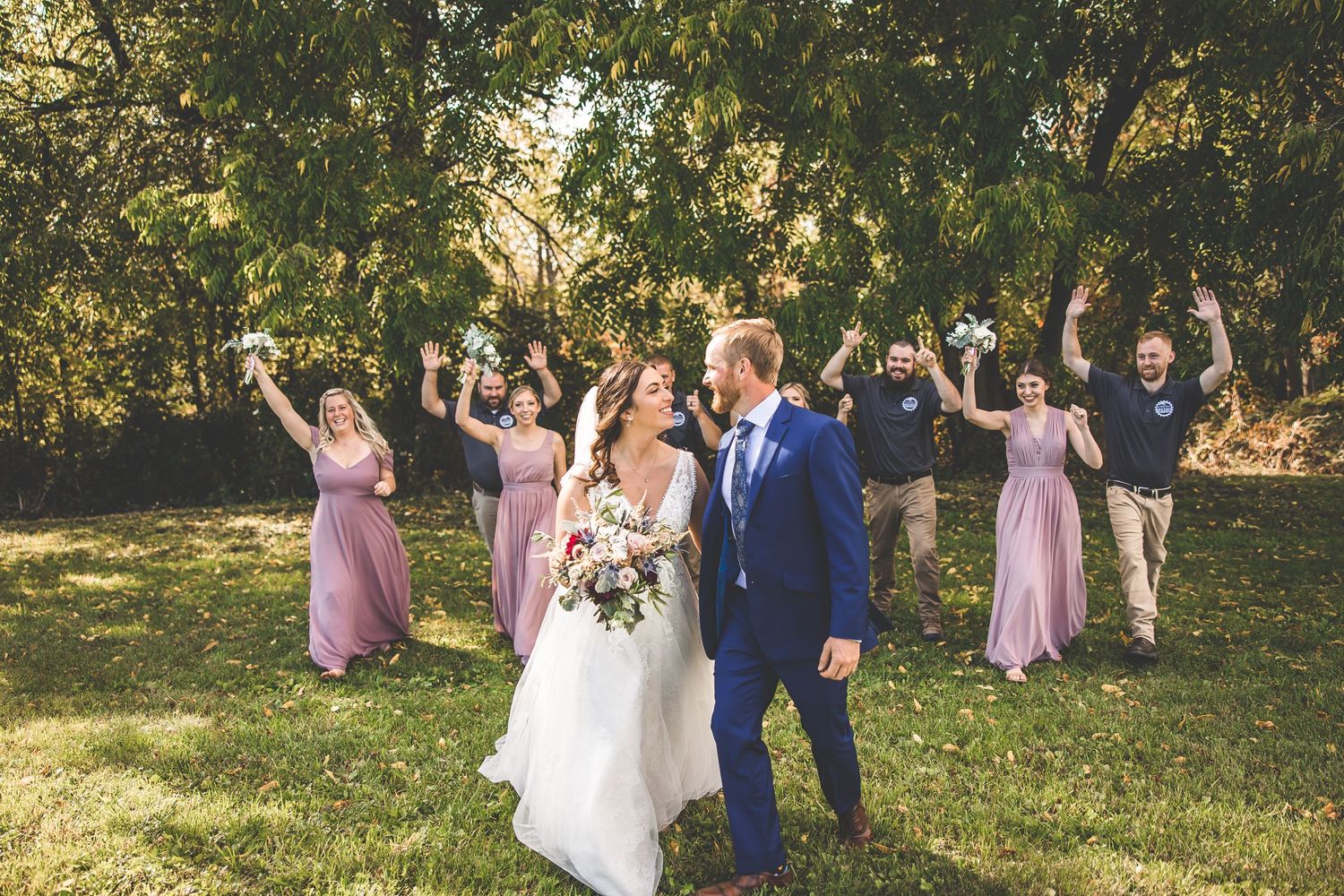 Wedding party celebrates with arms raised during outdoor photo session.