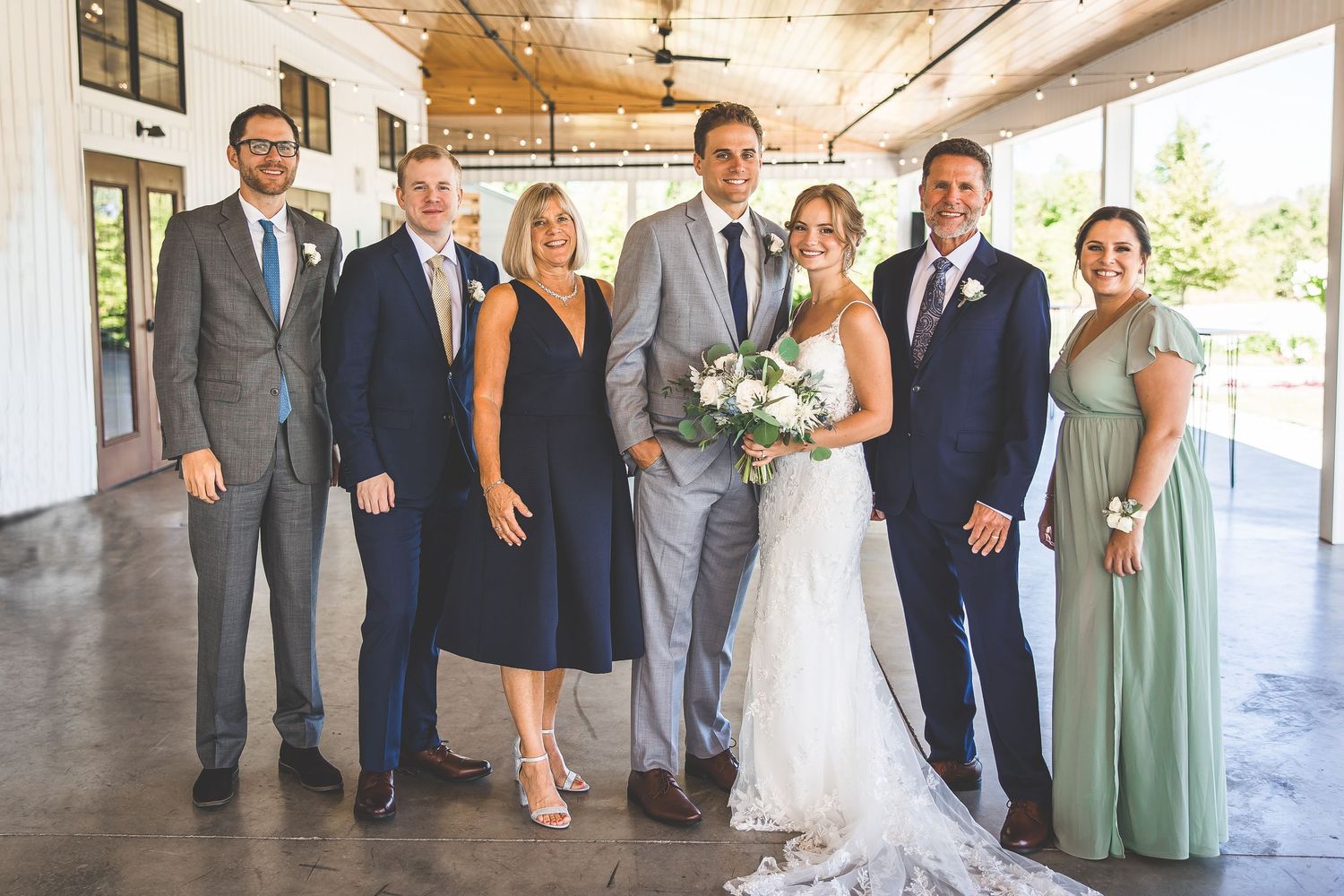 Wedding party members in navy and sage green attire pose together in an elegant covered outdoor venue.