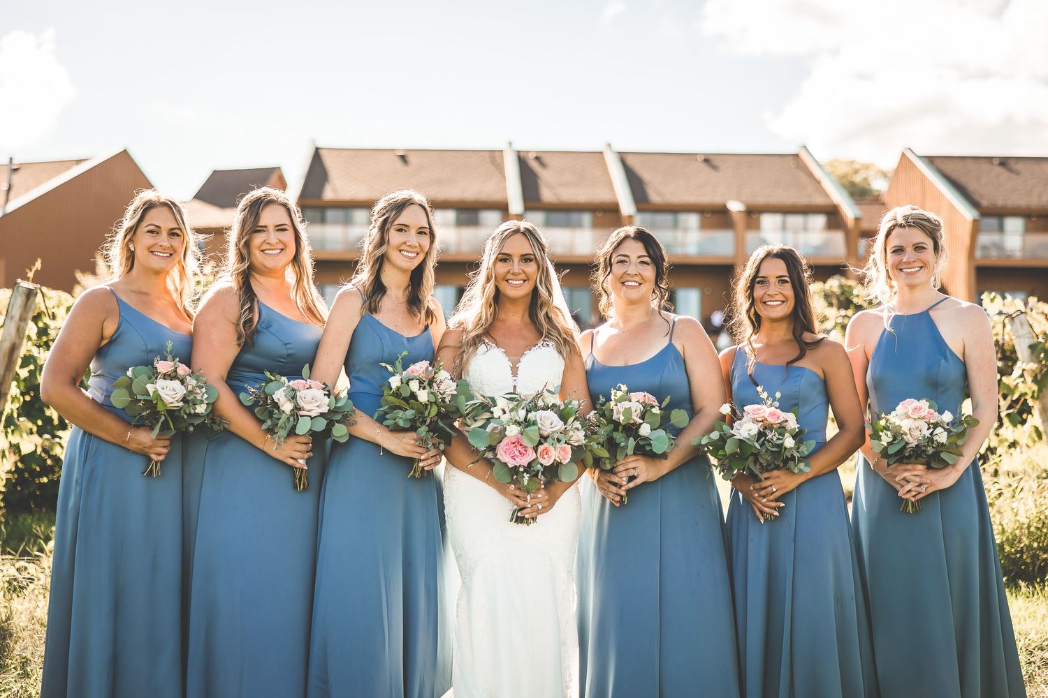 Bridesmaids in matching blue dresses pose together for wedding photos with natural lighting.