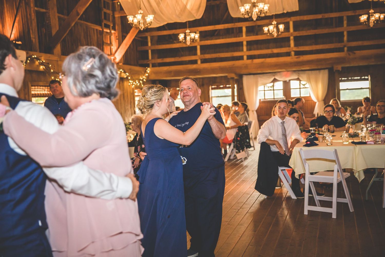Wedding reception dance floor in a rustic wooden barn with string lights overhead.