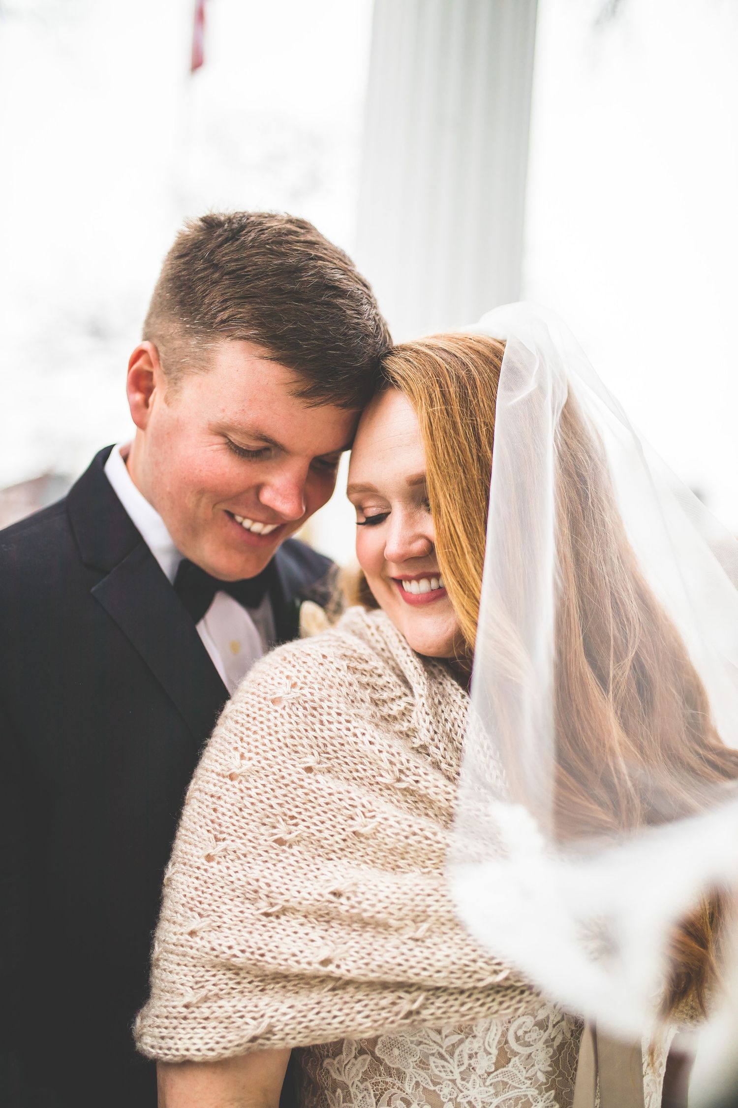 Intimate wedding portrait with bride wearing cream knit shawl against white columns.