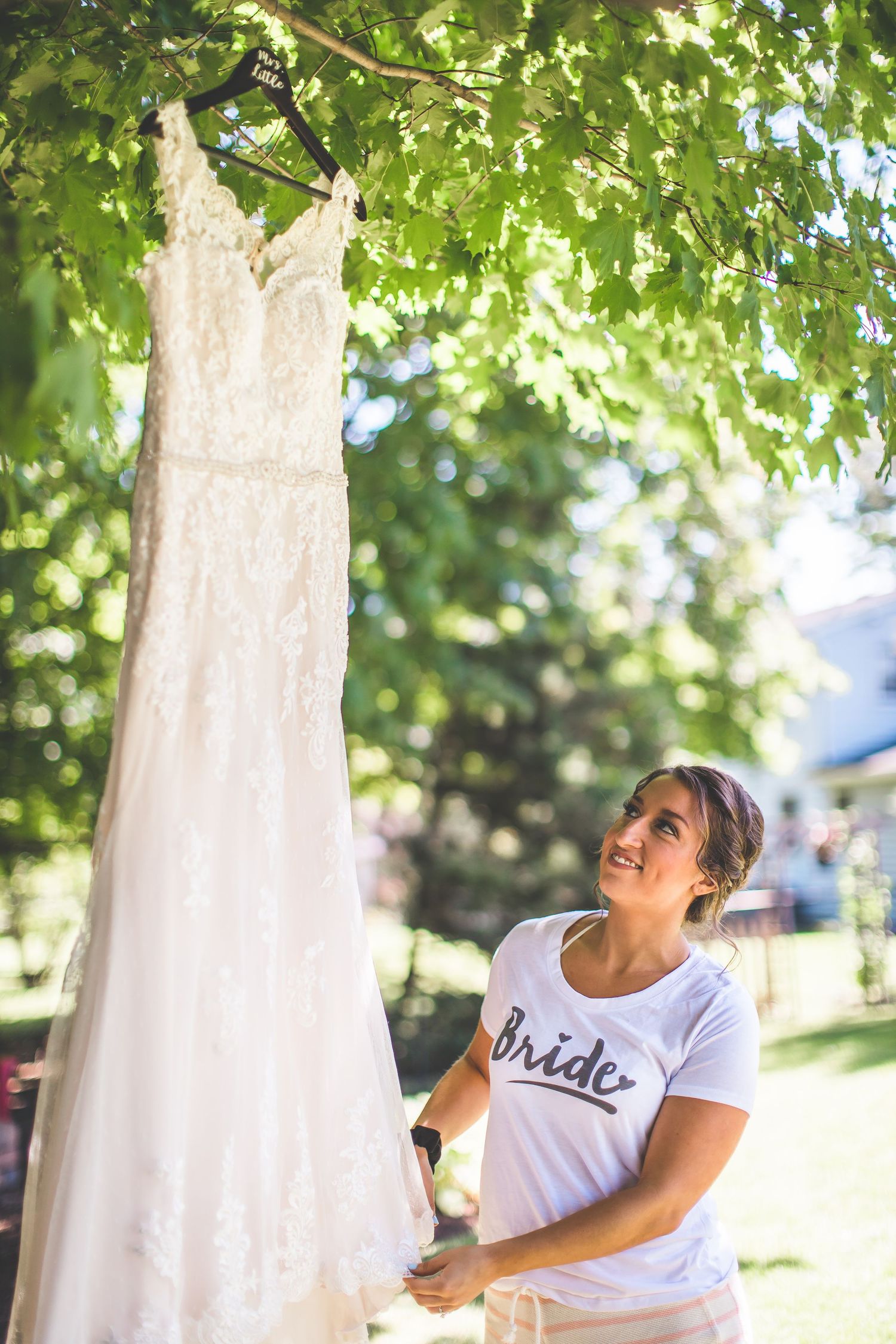 White wedding dress hanging from tree branches with sunlight filtering through green leaves.