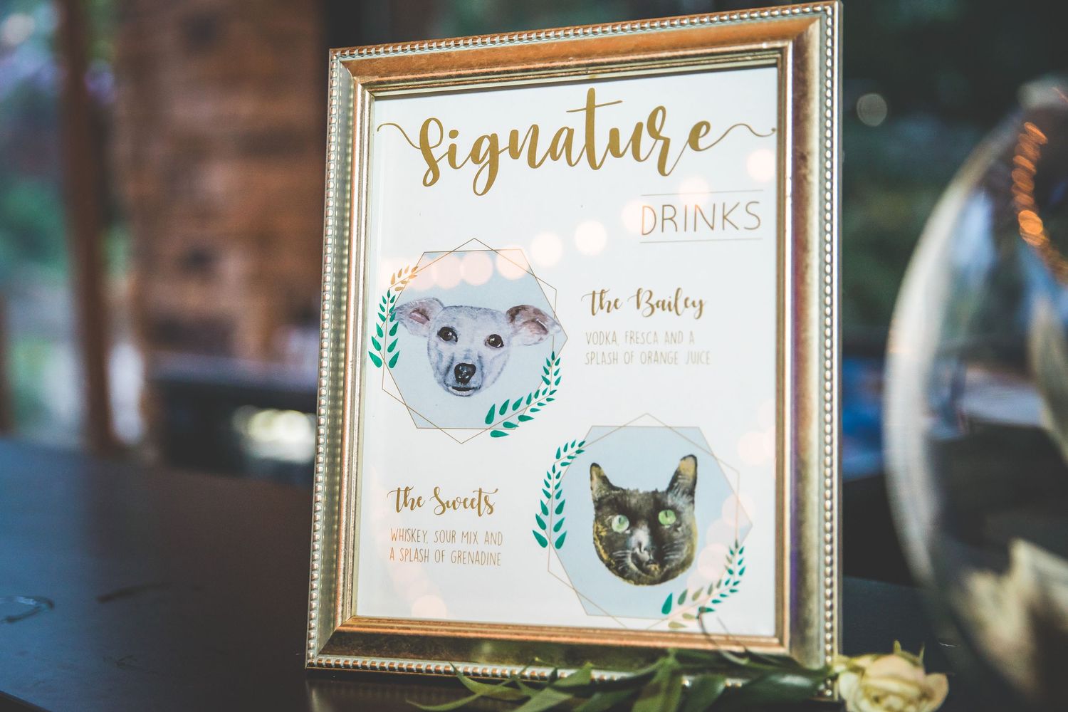 Framed signature cocktail menu with watercolor pet illustrations in gold frame.