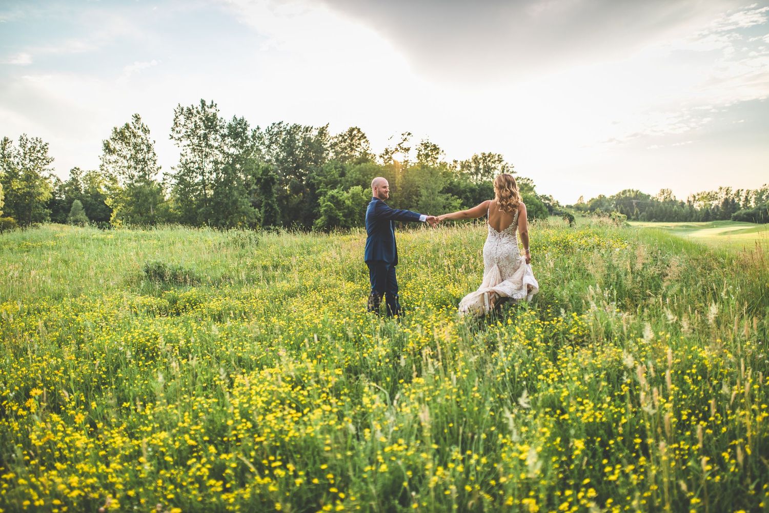 Couple walking through a field of yellow wildflowers at sunset.