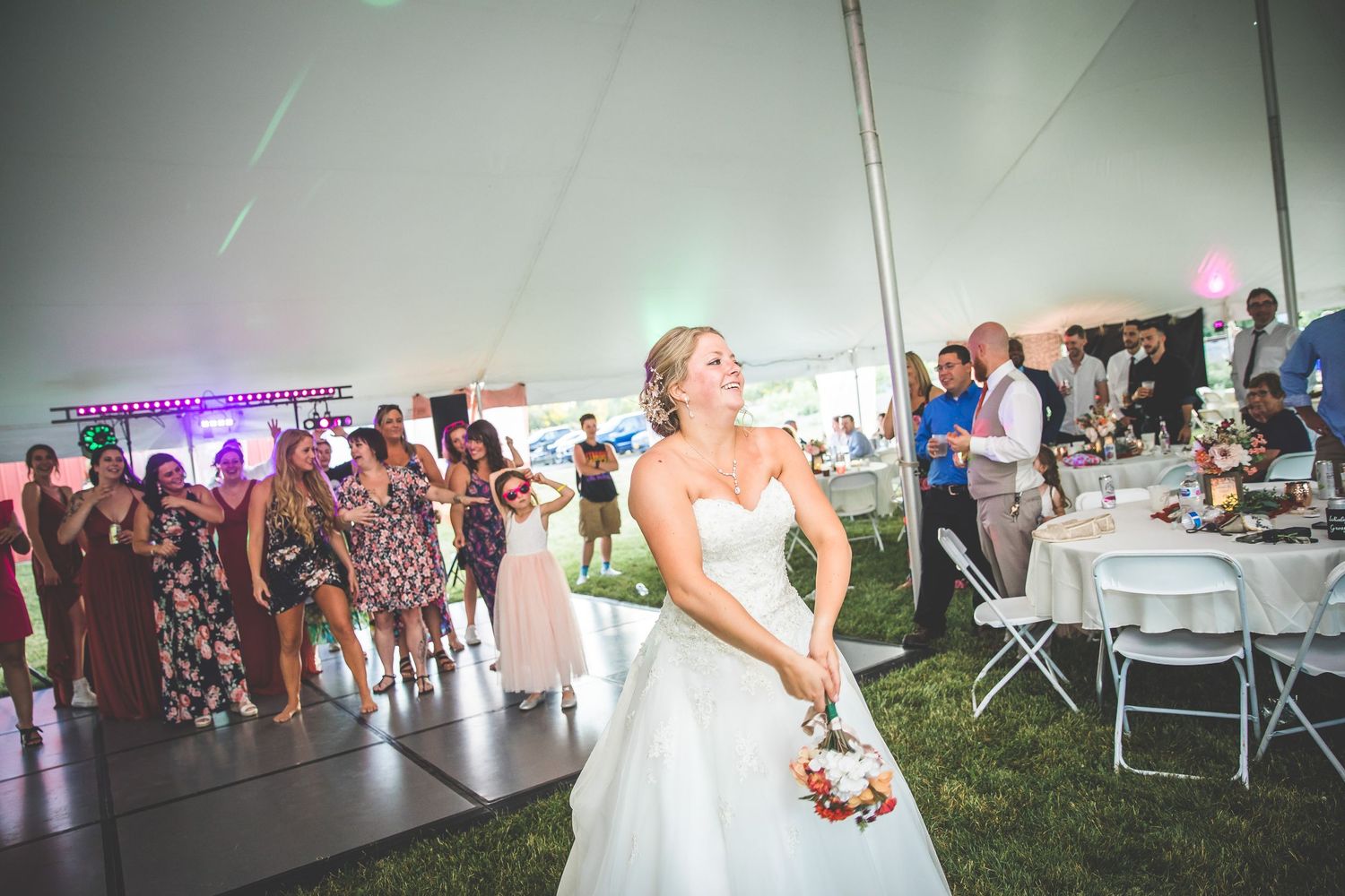 Bride preparing to toss her bouquet under a wedding tent with guests watching.