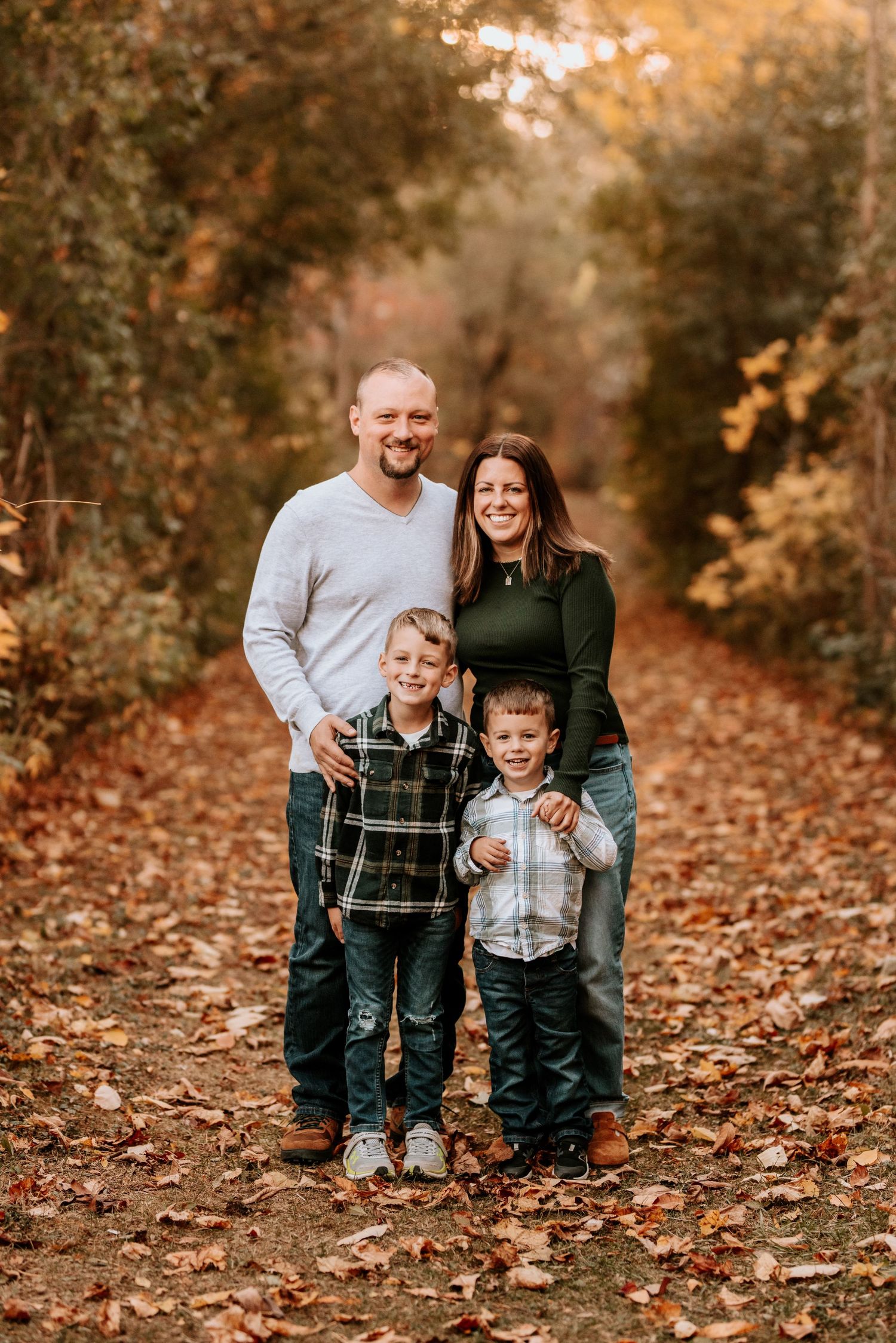 Family laughing together while posing on autumn leaves in wooded setting.
