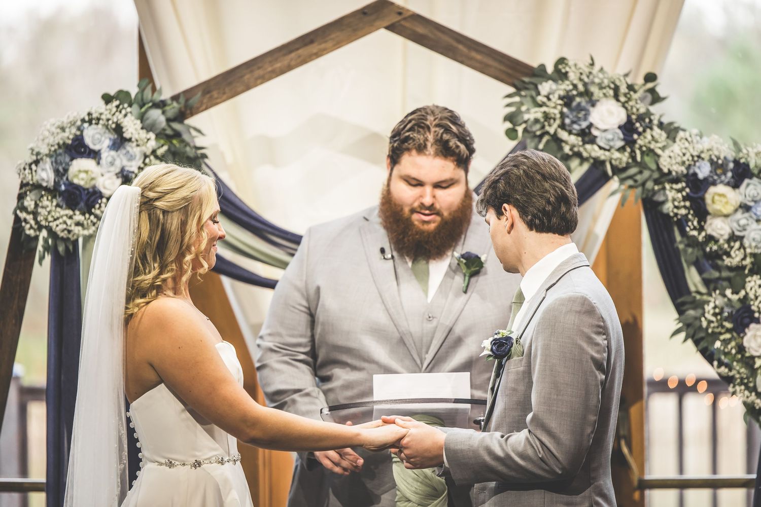 Wedding ceremony moment captured in rustic venue with decorative greenery and wooden beams.