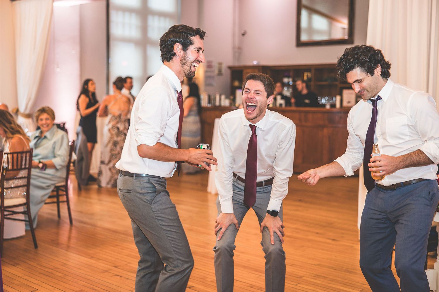 Wedding guests dancing and celebrating on wooden dance floor at reception.