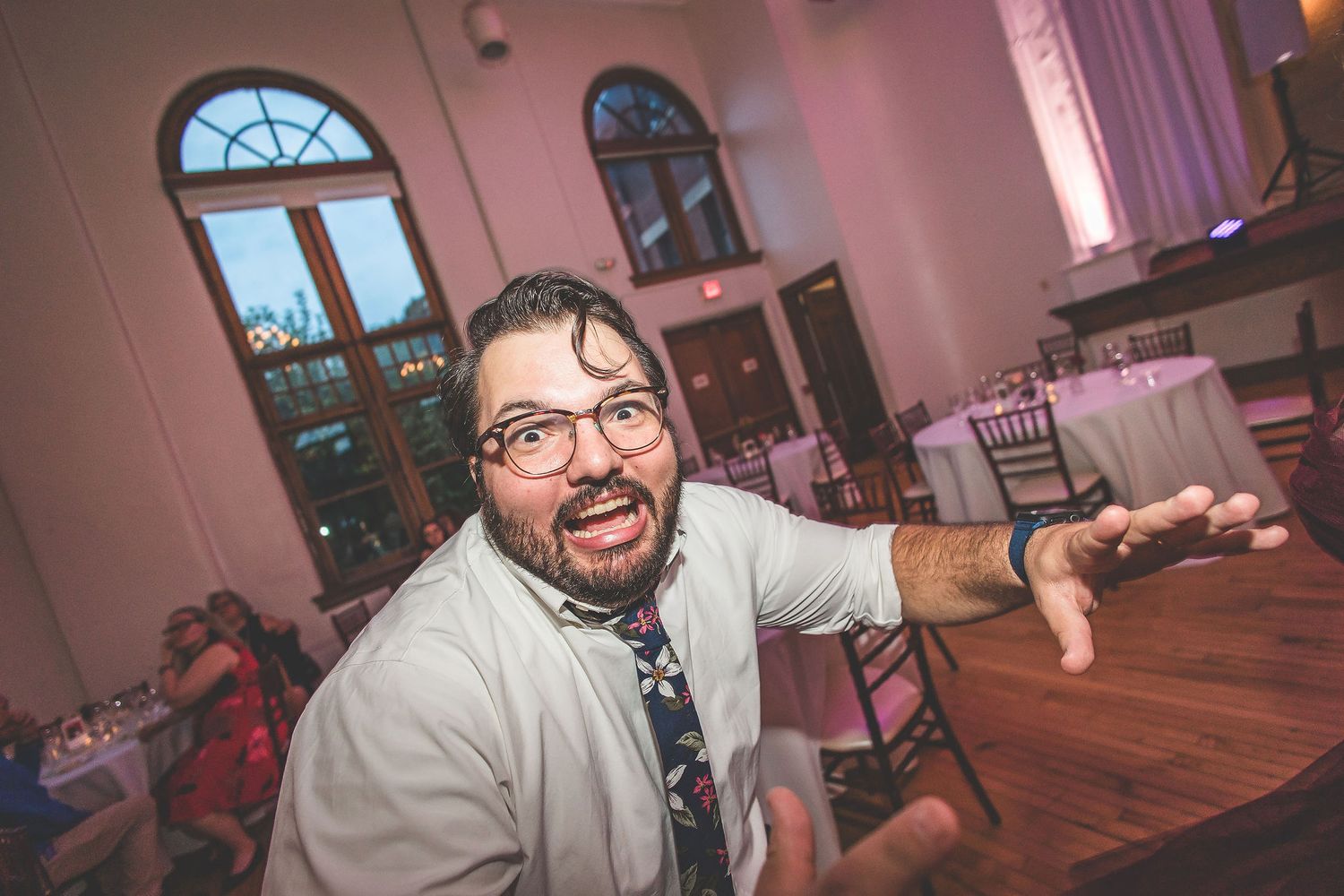 Wedding guests dancing and celebrating on a wooden dance floor under ornate chandeliers.