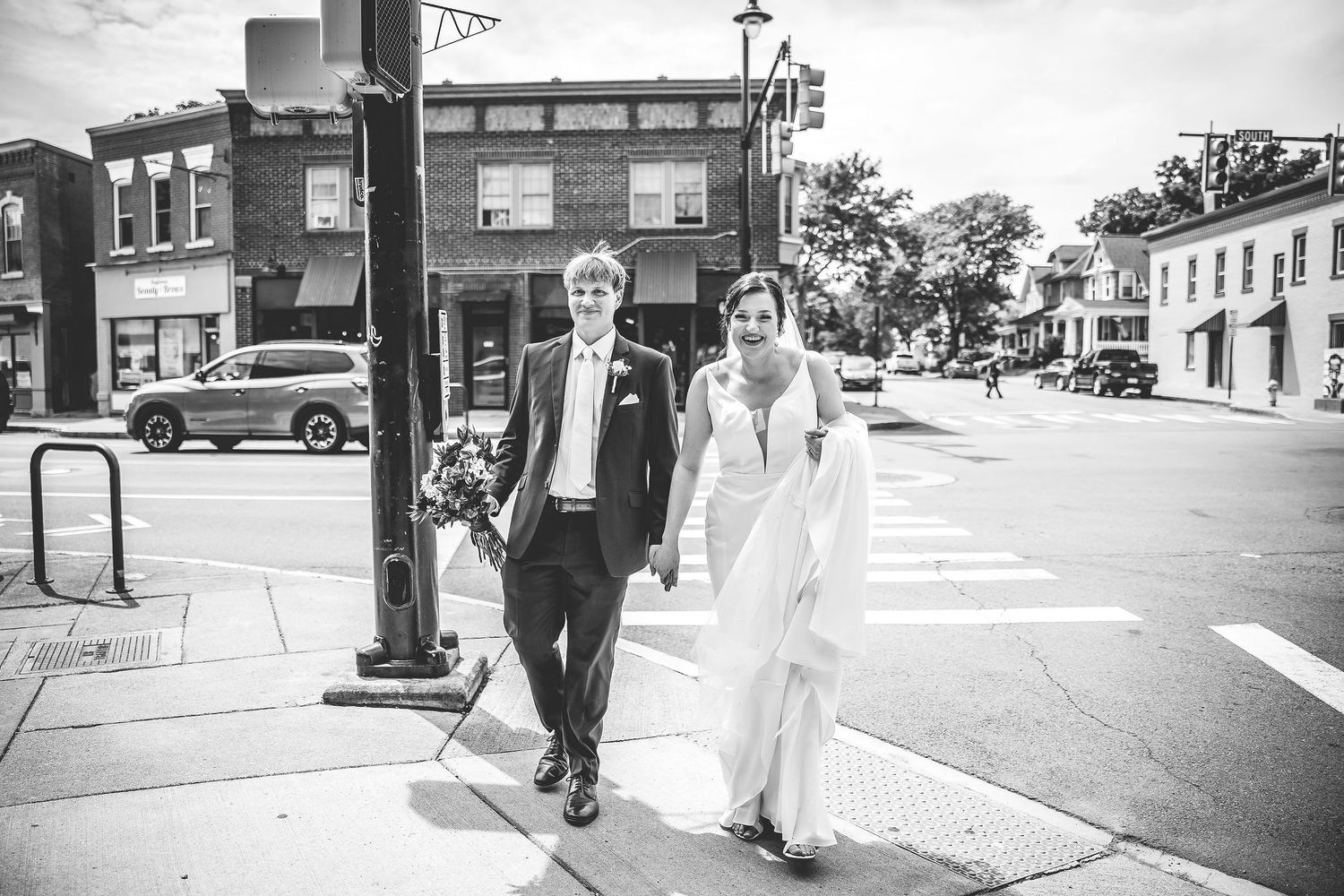Wedding couple walking along a small town main street with historic brick buildings.
