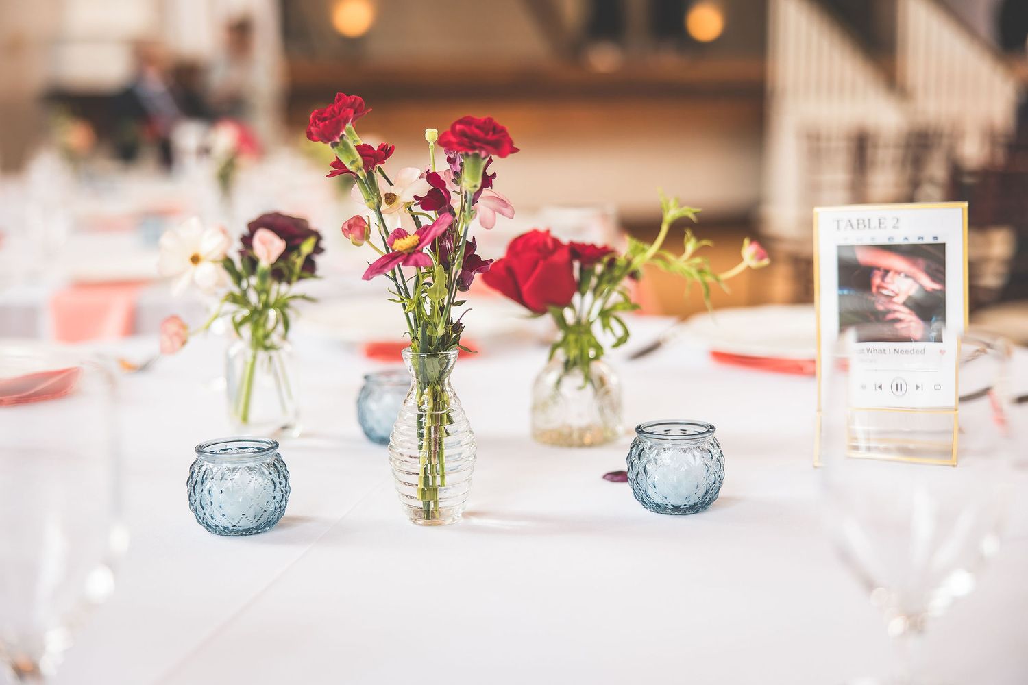Wedding reception table settings with blue glass vases and floral centerpieces.