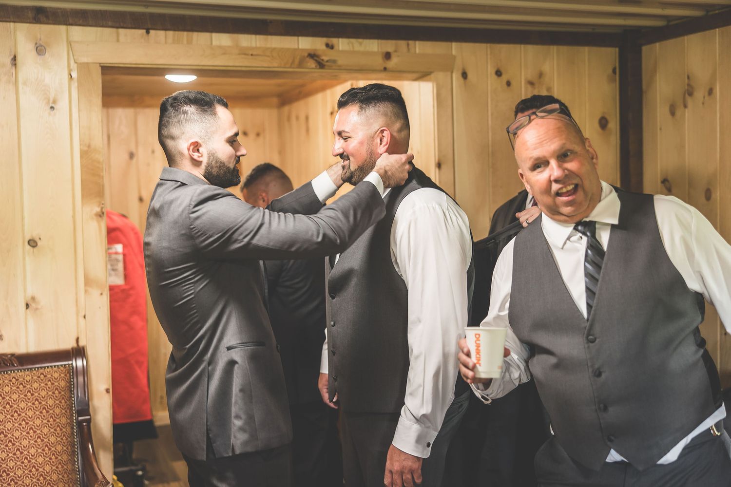 Wedding party members helping with formal attire preparations in wooden room.