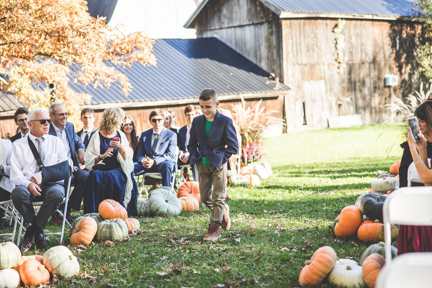 Fall wedding ceremony setup with pumpkins and rustic barn in background.