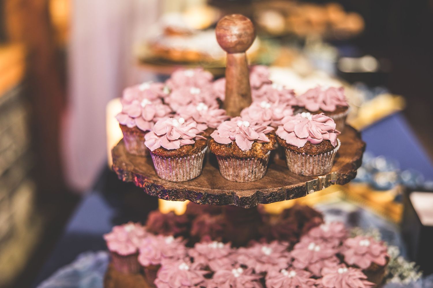 Pink frosted cupcakes and desserts arranged on tiered display stands at an elegant wedding reception.
