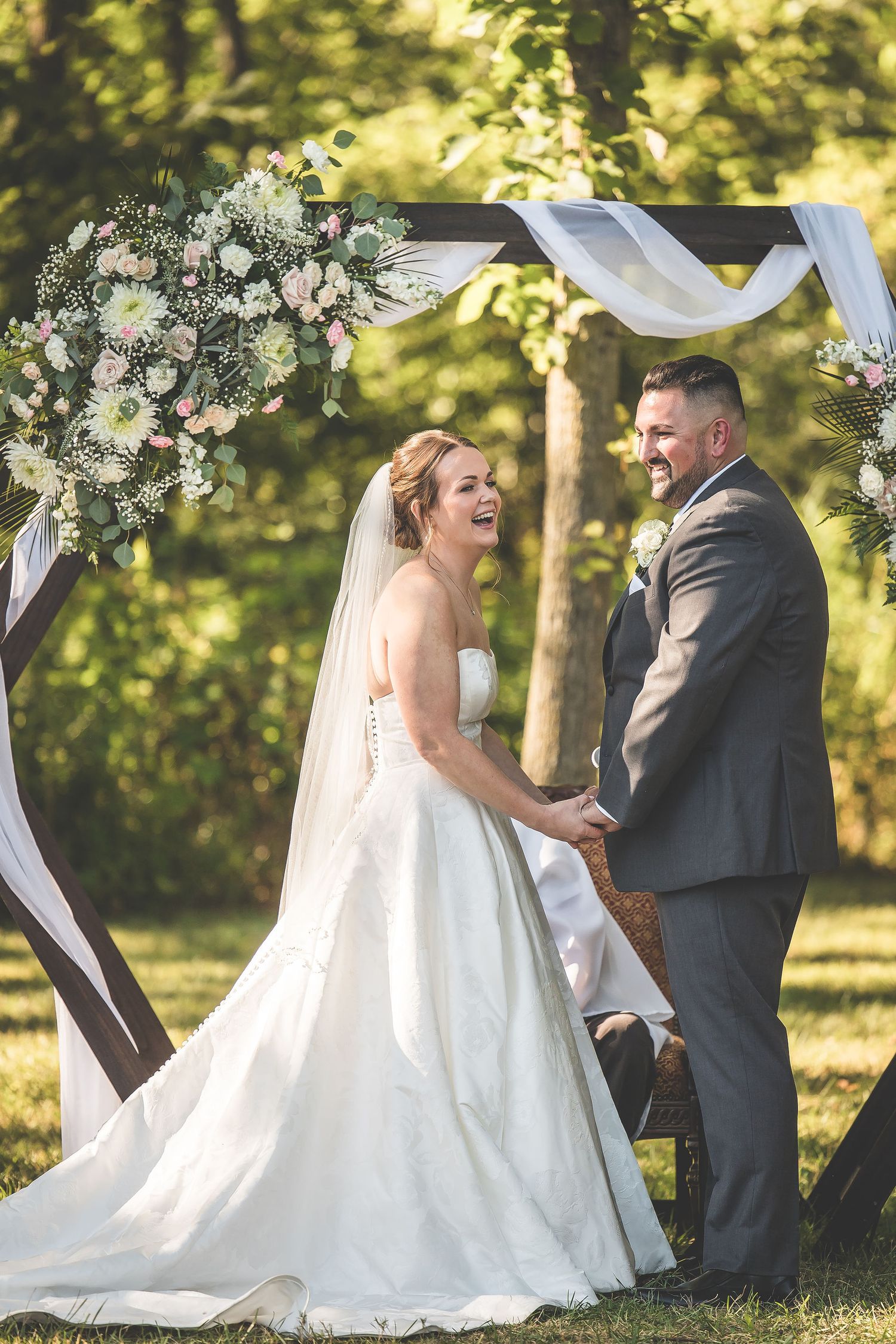 Joyful moments during wedding ceremony under white fabric arch in sunlit garden.