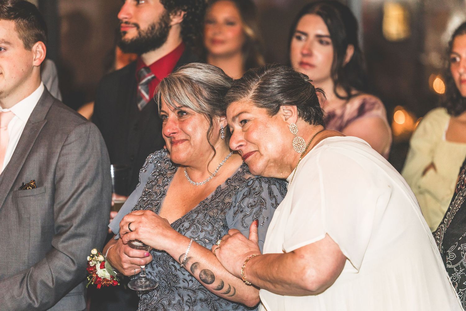 Wedding reception guests share emotional moments under warm lighting.