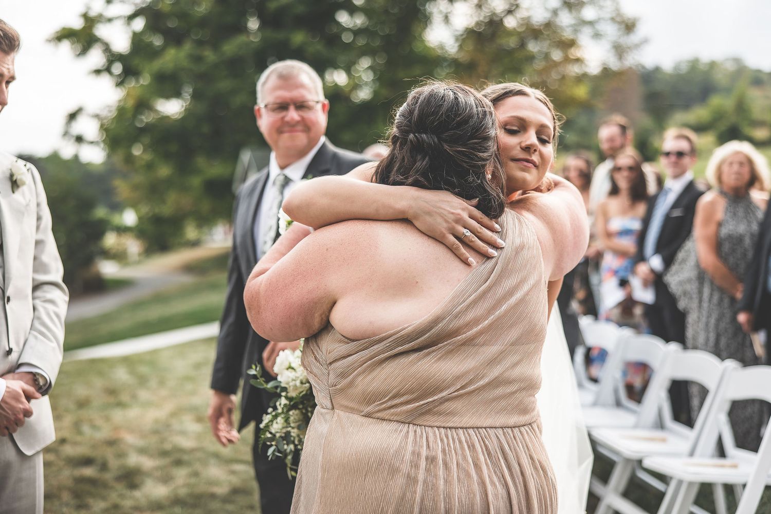 Wedding guests share emotional embraces during an outdoor ceremony celebration.
