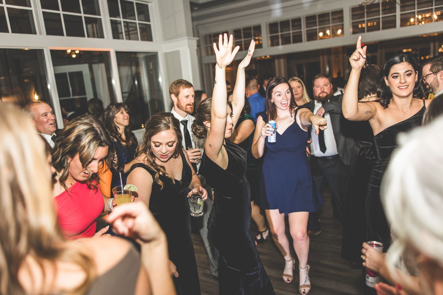 Energetic wedding guests dancing with raised arms on a crowded reception dance floor.