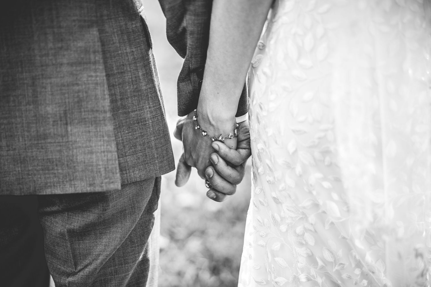 Black and white close-up of newlyweds holding hands showing wedding rings.