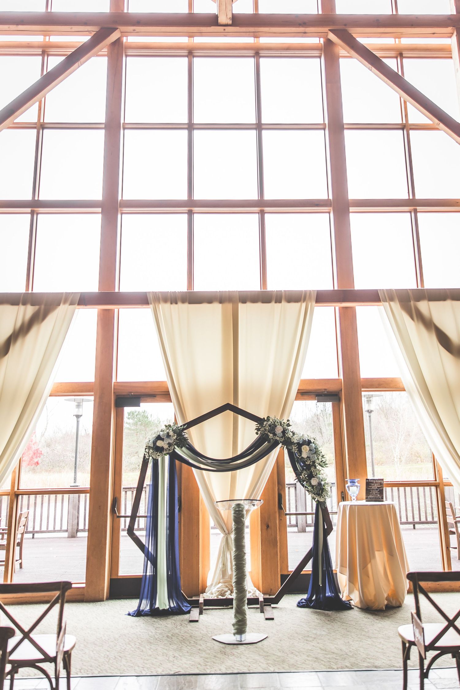 Wedding ceremony arch with navy and white draping in front of large windows.