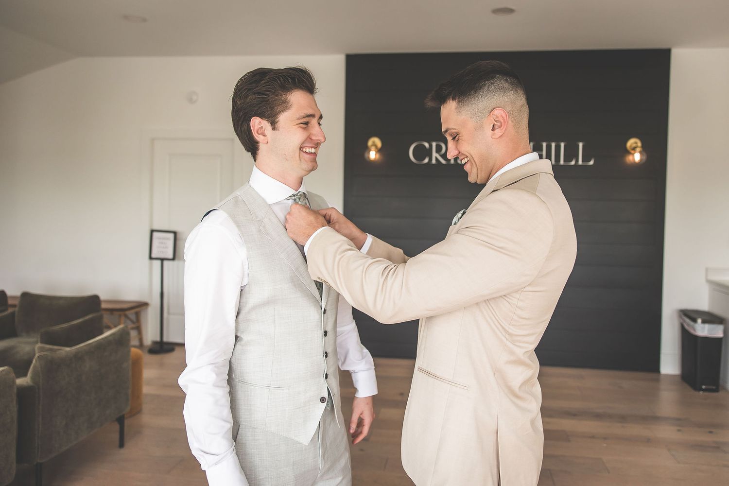 Wedding party members in light colored suits helping each other get ready before the ceremony.