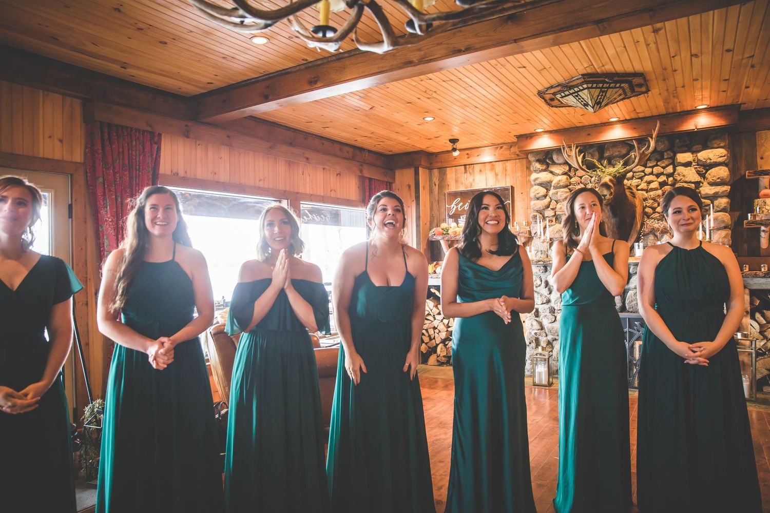 Bridesmaids in teal dresses stand in a row inside a rustic wooden venue.